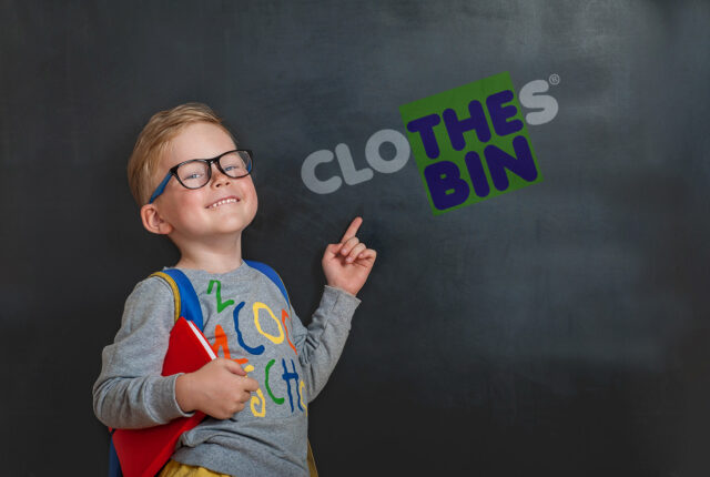 Student pointing at Clothes Bin logo on a chalkboard
